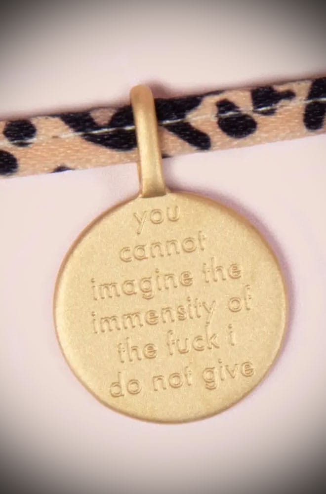 This charm tie bracelet features a stainless-steel, gold-plated charm engraved with "You Cannot Imagine the Immensity of the Fuck I Do Not Give". The sassy, round charm hangs on a leopard print fabric adjustable tie band.